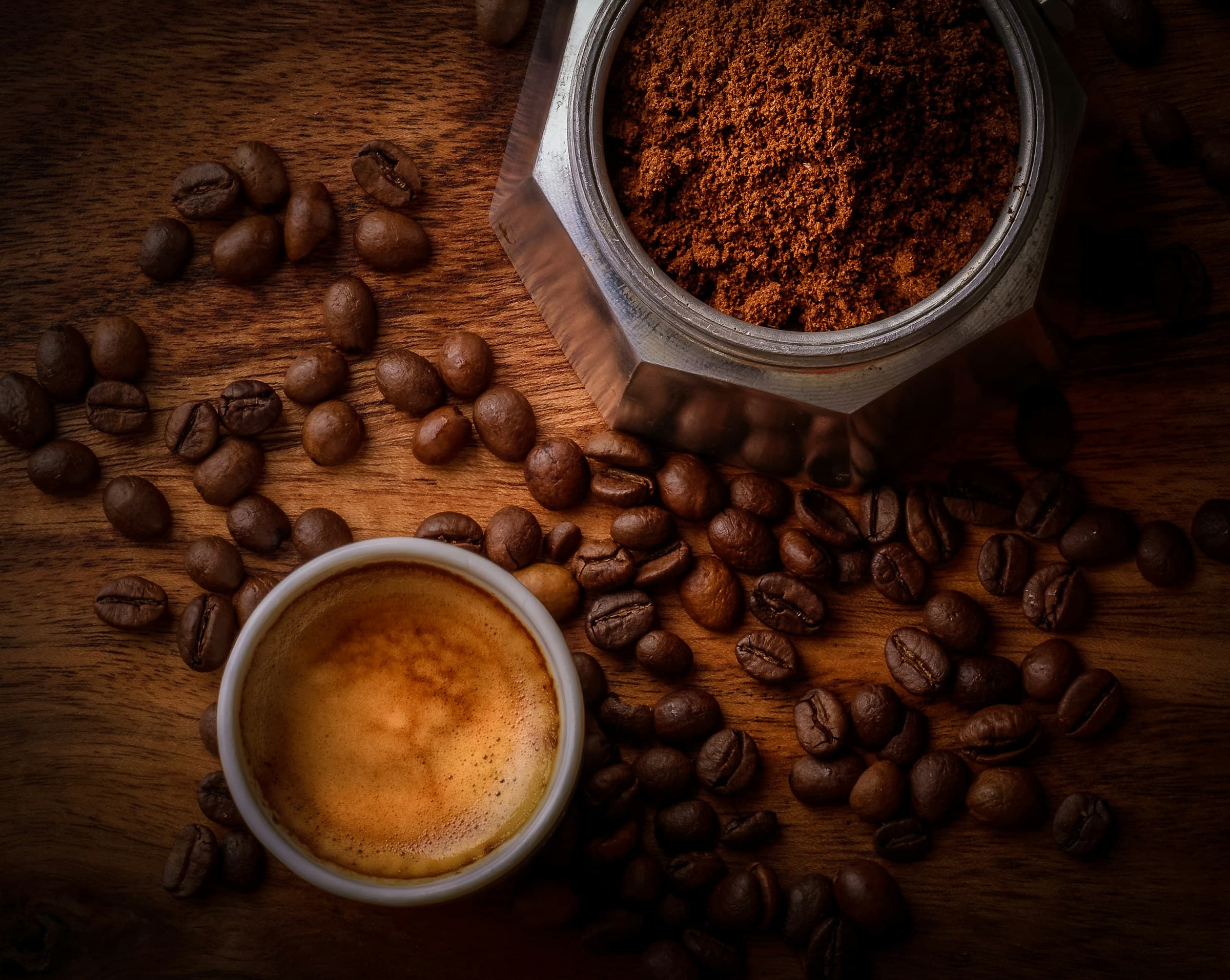 Espresso recién servido con crema, café molido y granos sobre una mesa de madera